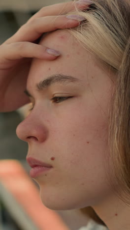 primer plano de una joven frotándose suavemente la frente con una expresión reflexiva, mostrando un momento de profunda contemplación, el fondo suavemente borroso