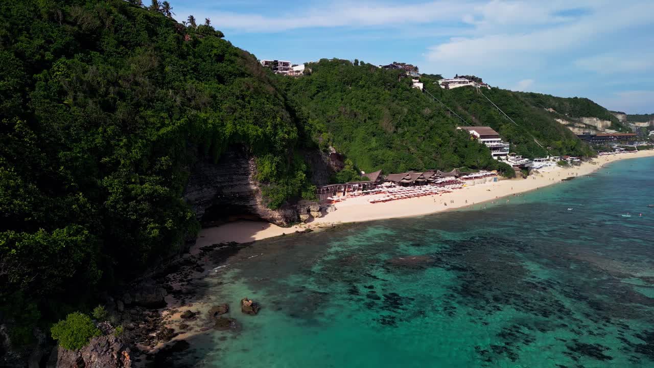 Captivating aerial perspective of Melasti Beach Uluwatu featuring vivid turquoise ocean tones, dramatic cliff lines, and natural coral reefs glowing under the tropical afternoon sun