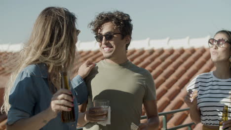 carefree friends talking together while eating pizza and drinking beer during a rooftop party