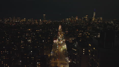 Aerial-panoramic-footage-of-illuminated-street-and-surrounding-buildings-at-night.-Cityscape-with-downtown-skyscrapers-in-distance.-Manhattan,-New-York-City,-USA