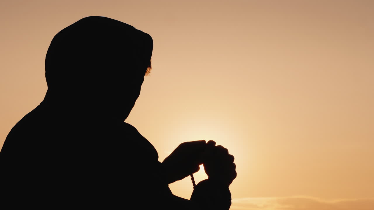 해질녘에 묵주를 통해 걸러내는 후드에 있는 남자의 실루엣