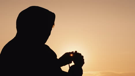 silhouette of a man in the hood sifting through the rosary at sunset