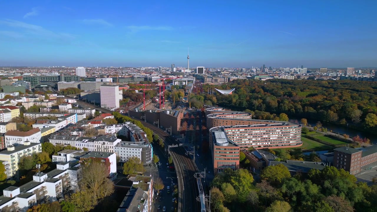 Vista panoramica di un treno che attraversa un ponte su un fiume a Berlino, circondato da un vibrante fogliame autunnale. Perfetta ripresa aerea con drone, volo inverso