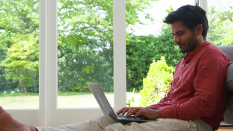 Primer-Plano-De-Un-Hombre-Trabajando-Desde-Casa-Sentado-En-El-Suelo-Del-Salón-Usando-Una-Computadora-Portátil