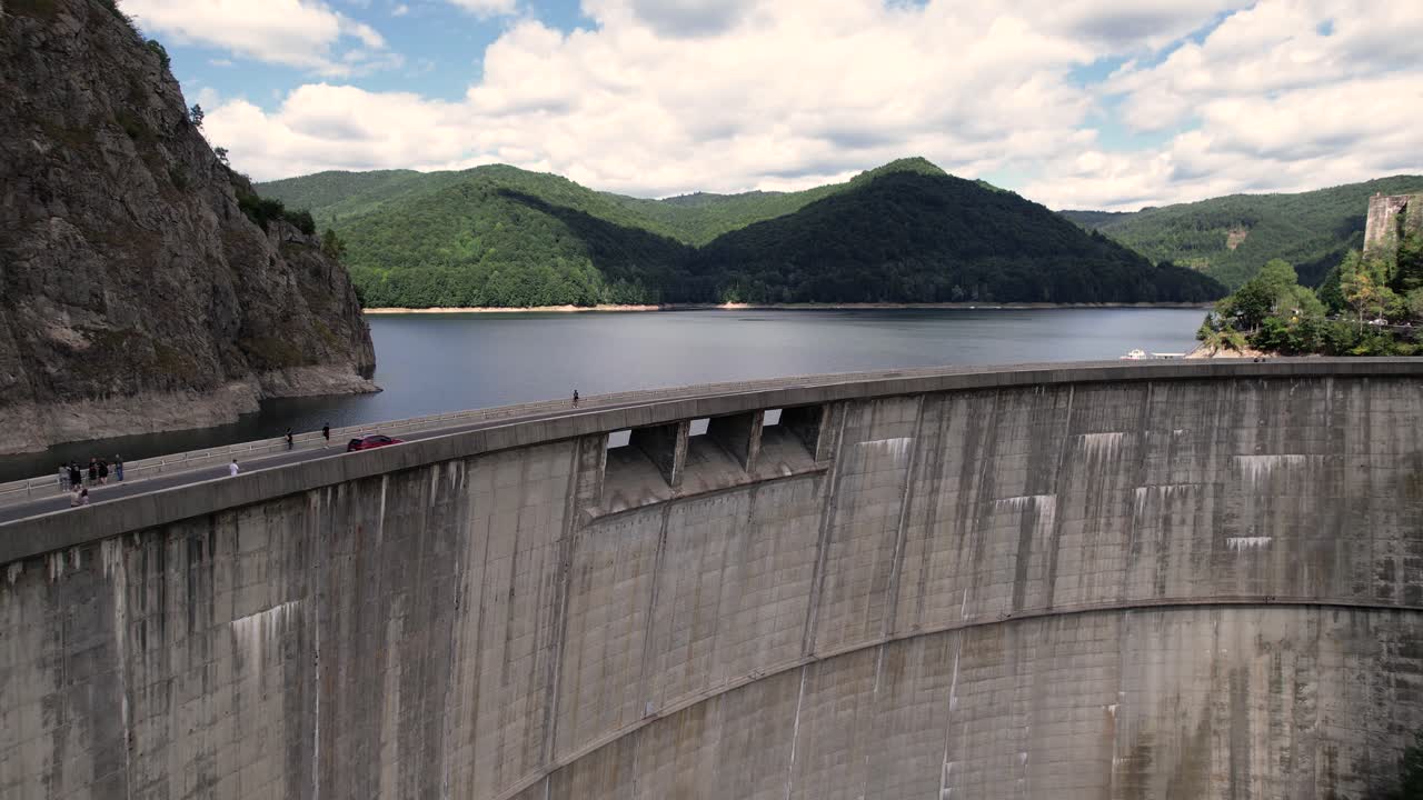 Aerial ascending shot revealing Vidraru Dam and lake in Romania. Blue lake, dramatic curves, and green mountain backdrop in 4K.