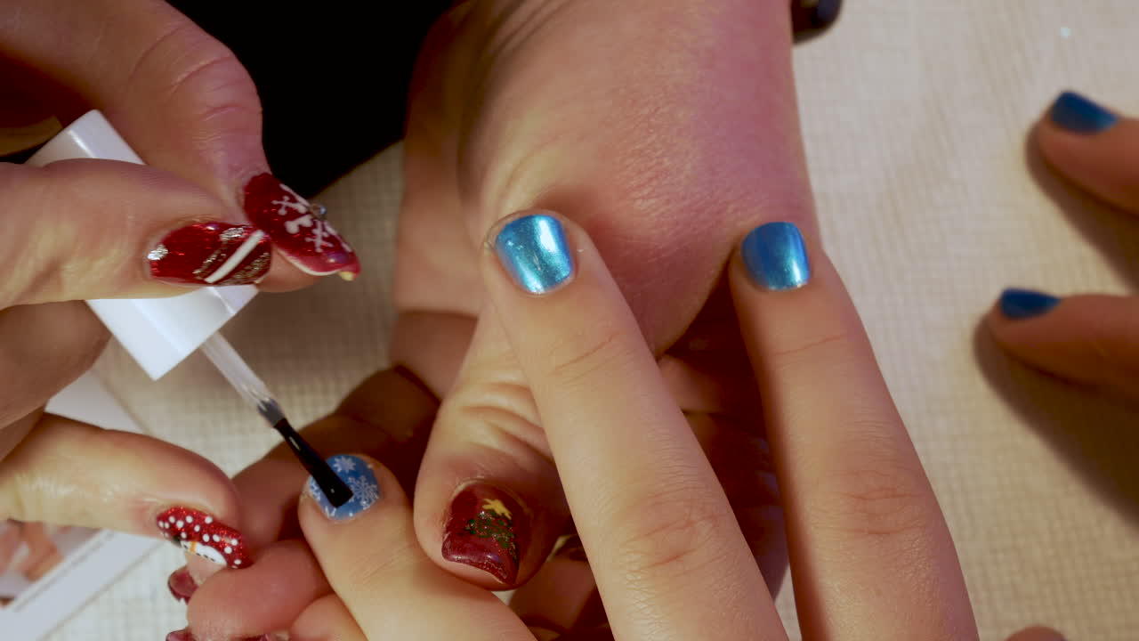 Manicurist applies a clear coat polish to a young girl's finger nails - close up Christmas designs