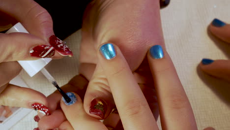 manicurist applies a clear coat polish to a young girl's finger nails - close up christmas designs