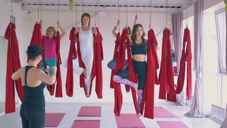 women-practice-fly-yoga-tree-asana-holding-red-hammocks