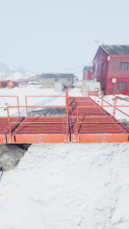 un puente de metal rojo que conduce a un edificio en un paisaje nevado