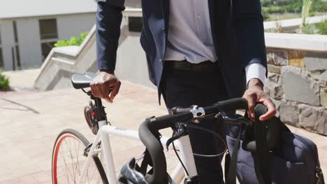 African-american-businessman-walking-and-holding-bike,-slow-motion