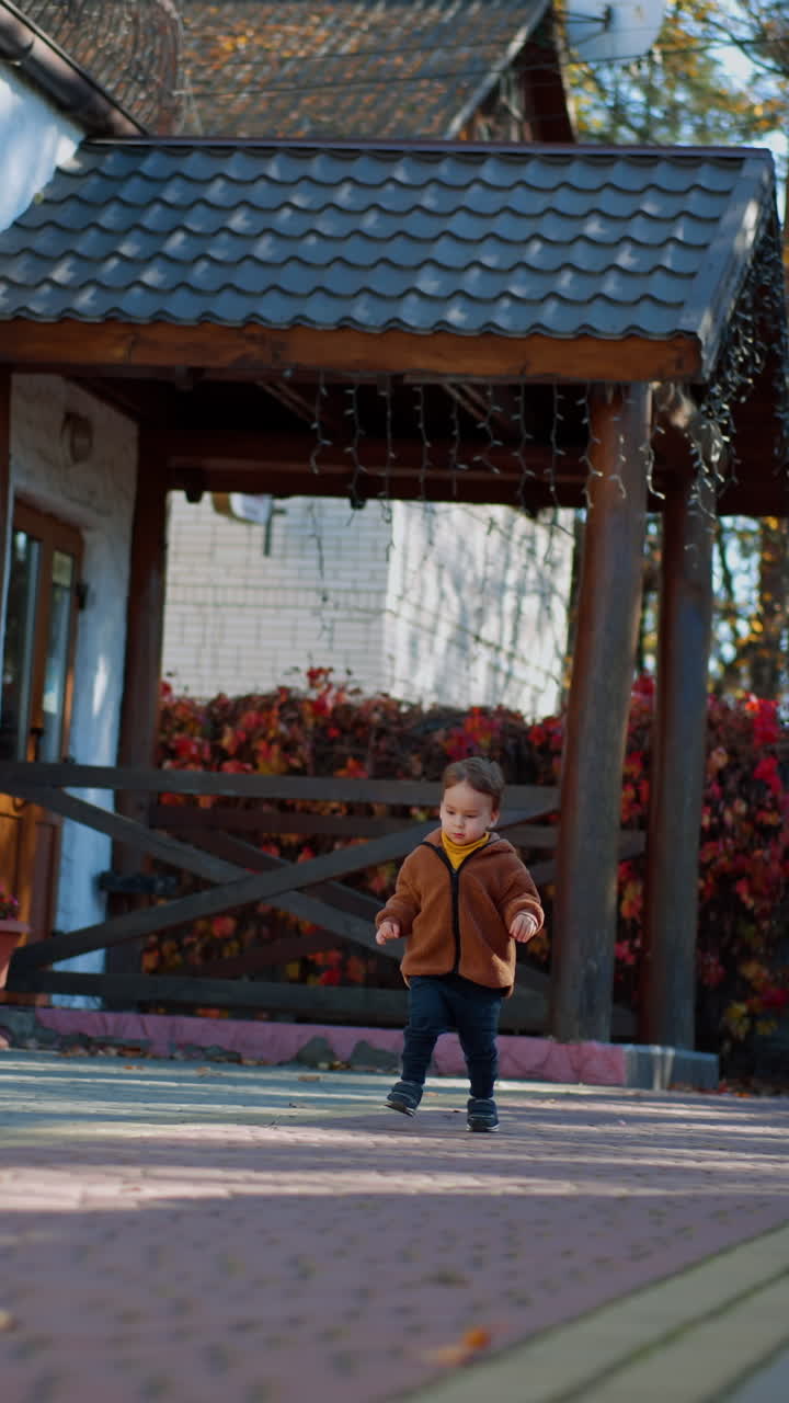 Caucasian toddler wearing brown jacket and blue pants runs outdoors. Good time outside in autumn. Vertical video