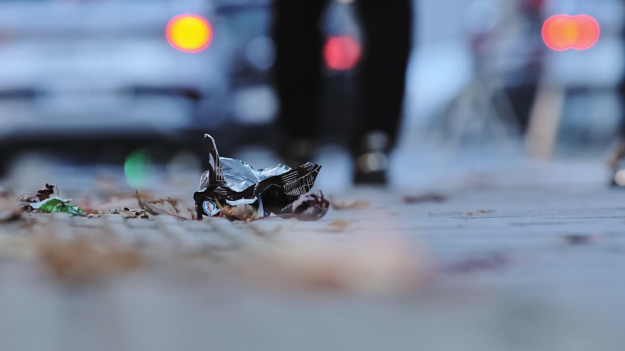 Close-up of crushed plastic garbage on urban path with blurred people and cars