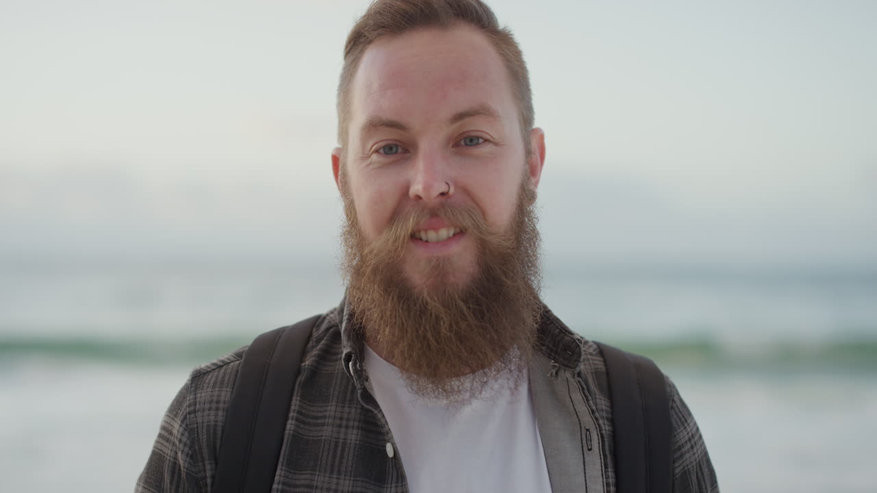 retrato de un joven barbudo sonriendo mirando a la cámara en la playa disfrutando de un estilo de vida positivo apuesto hombre hipster en la playa