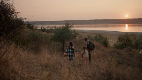 Vista-Trasera-De-Una-Niña-Morena-Con-Una-Camisa-A-Cuadros-Verde-Junto-Con-Su-Esposo-Moreno-Y-Su-Pequeña-Hija-Caminando-Por-La-Colina-Después-De-Su-Picnic-Fuera-De-La-Ciudad-En-La-Tarde-De-Verano.