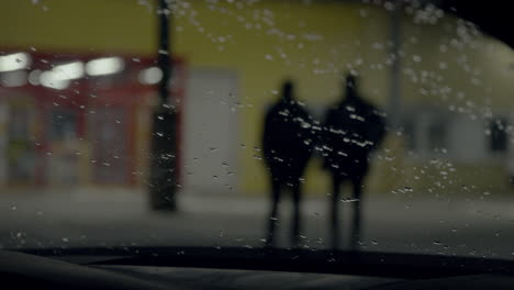 Silueta-De-Chicos-Caminando-Por-La-Noche-Filmada-A-Través-Del-Parabrisas-Del-Camión-Con-Gotas-De-Lluvia