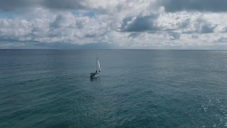 A-Stunning-Aerial-Drone-Shot-of-a-Sailing-Yacht,-Gazing-Out-at-the-Vast,-Endless-Horizon-Over-Winding-Waters,-Dotted-with-Clouds-and-Waves-Against-a-Luminous-Blue-Sky-in-the-Caribbean-Sea,-Mexico