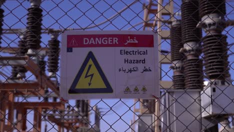 electrical safety warning: danger sign for electrical hazard in multiple languages on chain-link fence at power substation