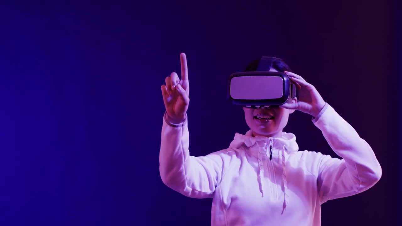 Asian woman using vr headset, touching virtual screen on blue background, copy space, slow motion