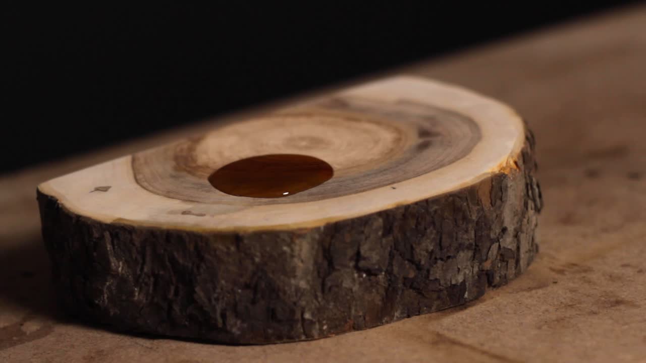 Close up of a carpenter pouring staining solution onto a sliced, thick piece of tree trunk that has been sanded down and is being finished