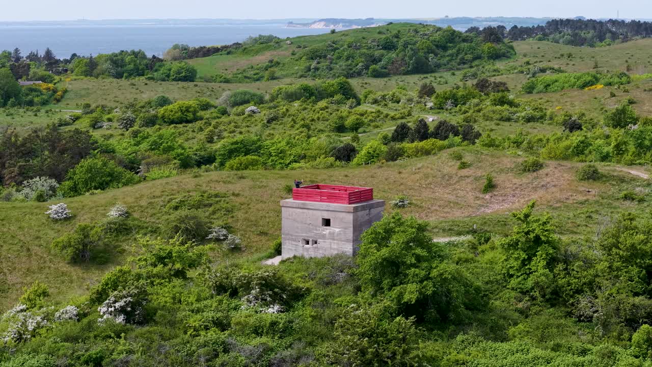 Aerial view of an old German World War II bunker with a red roof, surrounded by overgrown grass and coastal greenery
