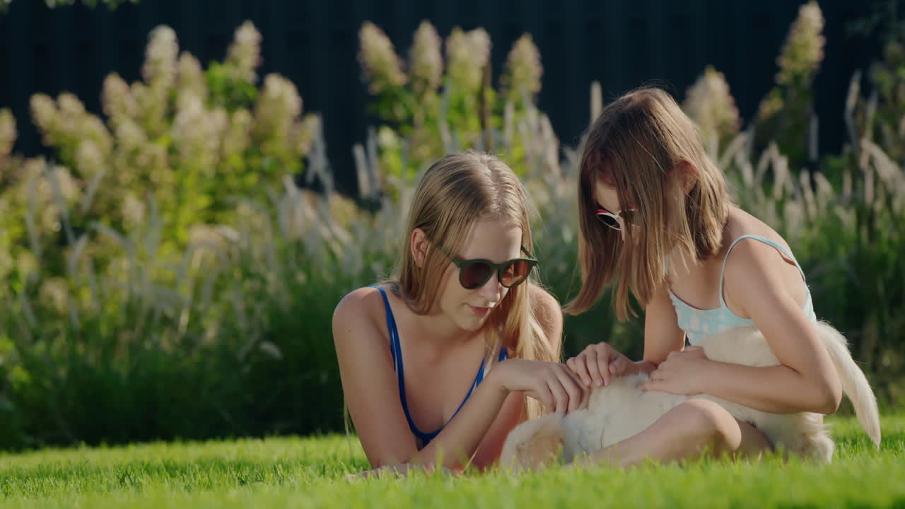 아이들은 집 뒷마당에서 강아지와 함께 놀고 있다. 초록색 잔디에 앉아 있다.