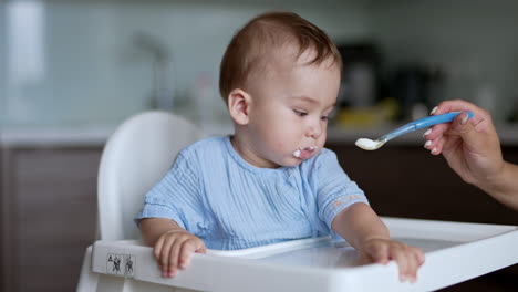 adorable little child being fed from spoon. cute nice baby takes the food and makes funny face. close up.