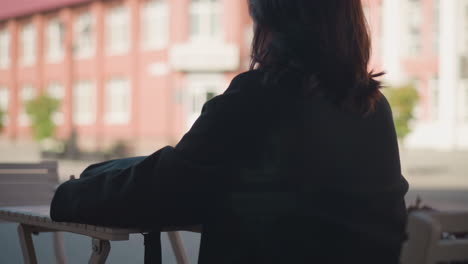 close-up side view of lady with ring-adorned fingers and polished nails carefully unzipping her black bag on a wooden table, revealing a laptop inside