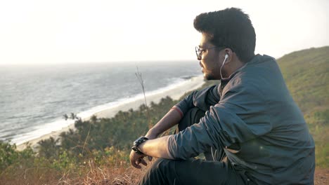 young happy man wearing jacket and eyeglasses enjoying a view of beautiful ocean and sunrise