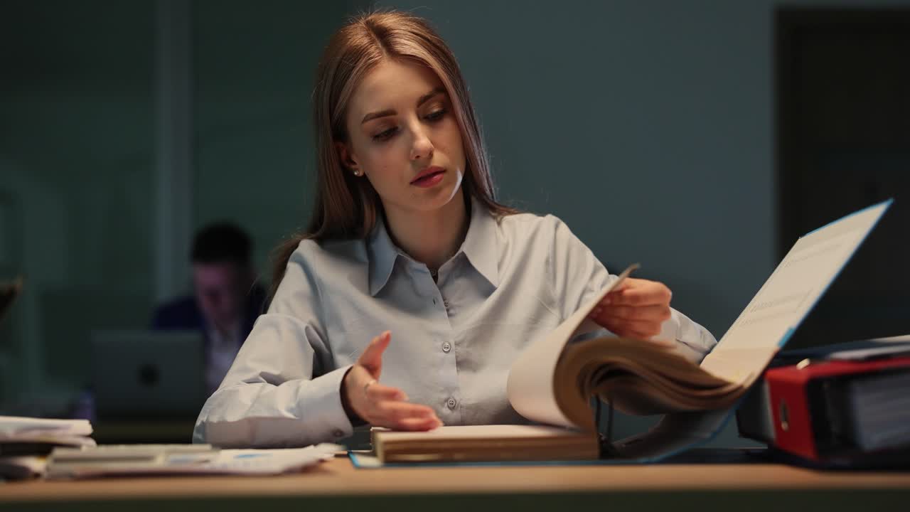 Jovem mulher trabalhando até tarde e revisando documentos em uma mesa de escritório