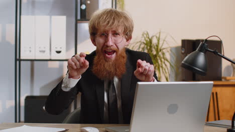 Business-man-working-on-office-laptop-pointing-to-camera-looking-with-happy-expression-making-choice