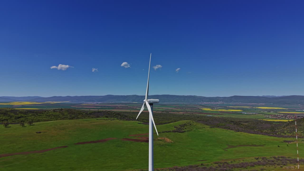 Turbina eolica che si erge alta in un paesaggio verde sotto un cielo azzurro e limpido