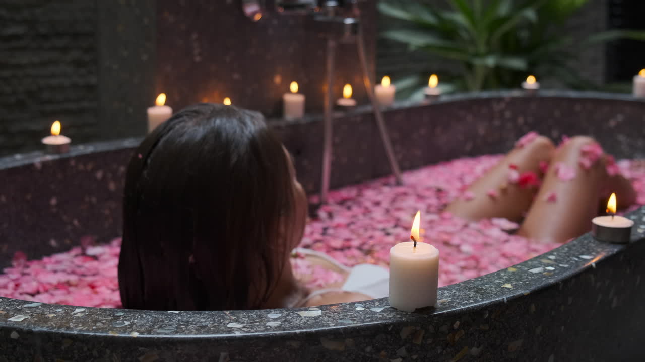 Woman enjoying a relaxing spa bath with candles and rose petals
