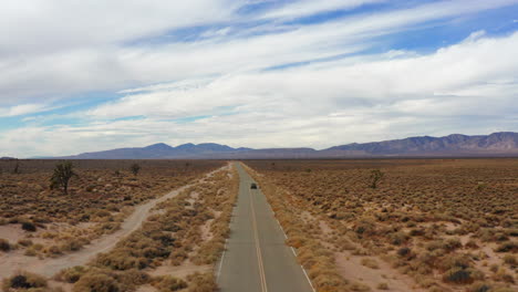 Fliegen-Weit-Hinter-Dem-Auto-Auf-Der-Mojave-Wüstenautobahn-In-Richtung-Berge-Und-Bewölktem-Himmel