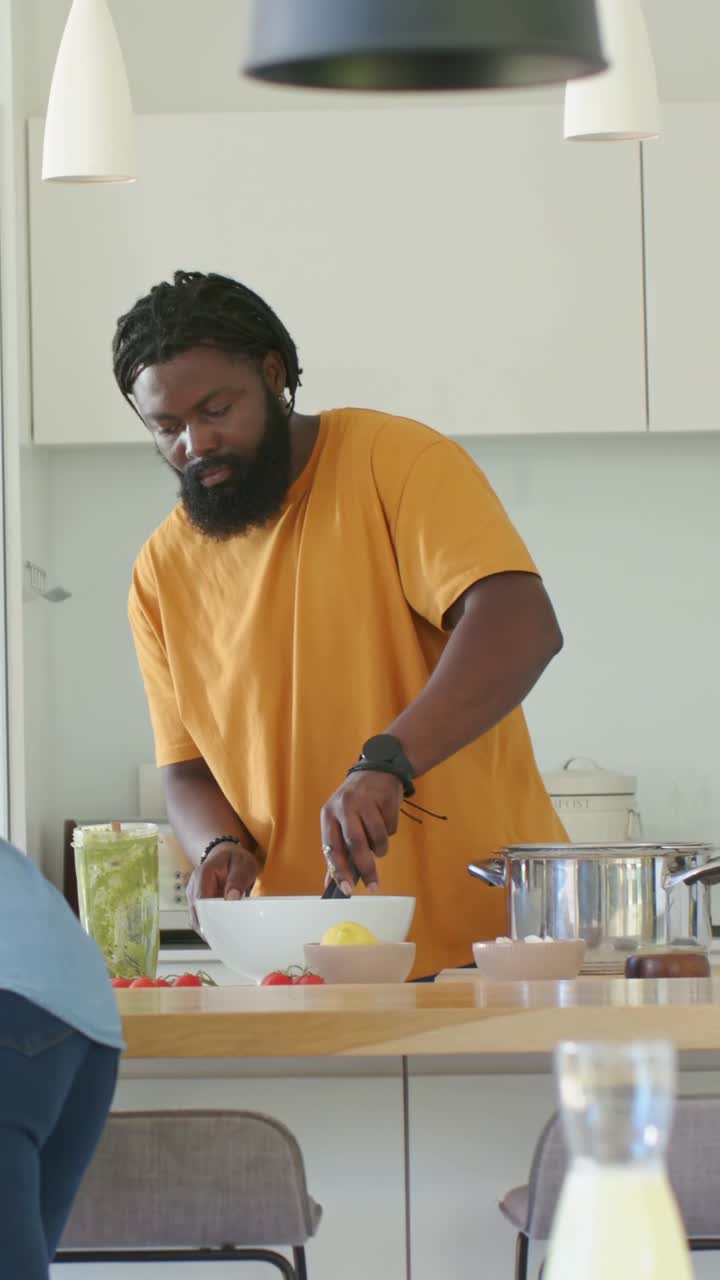 Vertikales Video: Mann kocht an der Kücheninsel, gibt Ei in Topf, schwenkt Schüssel für gemeinsames Essen