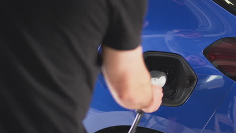 hombre cargando un coche eléctrico con un cable usando una aplicación en el teléfono para monitorear el nivel de carga de la batería