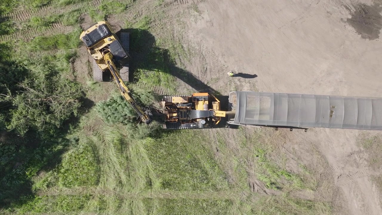 Wild trees getting transformed to minute particles by an automated machine in forest. Aerial view.