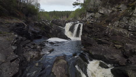 Drone-footage-flying-quickly-and-low-against-the-stream-in-the-river-towards-small-waterfall,-Rogie-Falls-Powerful-Waterfall-in-Scotland