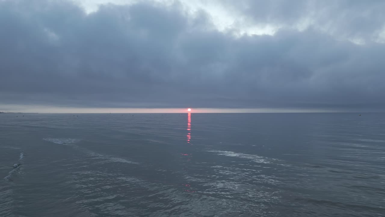 Witness the breathtaking beauty of a vibrant sunset illuminating the horizon over tranquil waves. Seagulls roam the skies as day transitions to night