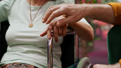 senior man comforts wife with disability in wheelchair while they talk to nurse