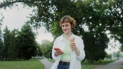 mujer comiendo helado y usando un teléfono en un parque