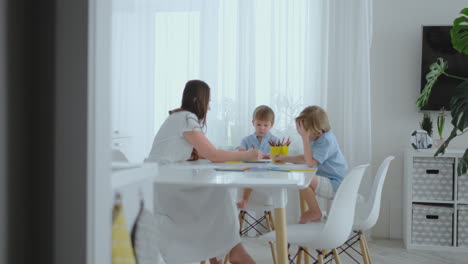 mamá y sus dos hijos sentados en la mesa de la cocina dibujando lápices de colores familia dibujando en el césped en el verano. los niños aprenden a dibujar, y mamá ayuda con el dibujo