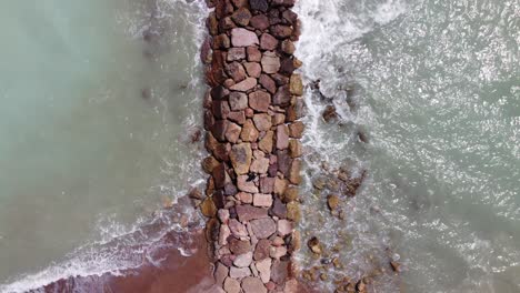 top down drone shot a person walking over a stone bridge, with blue water and waves crashing against the stone