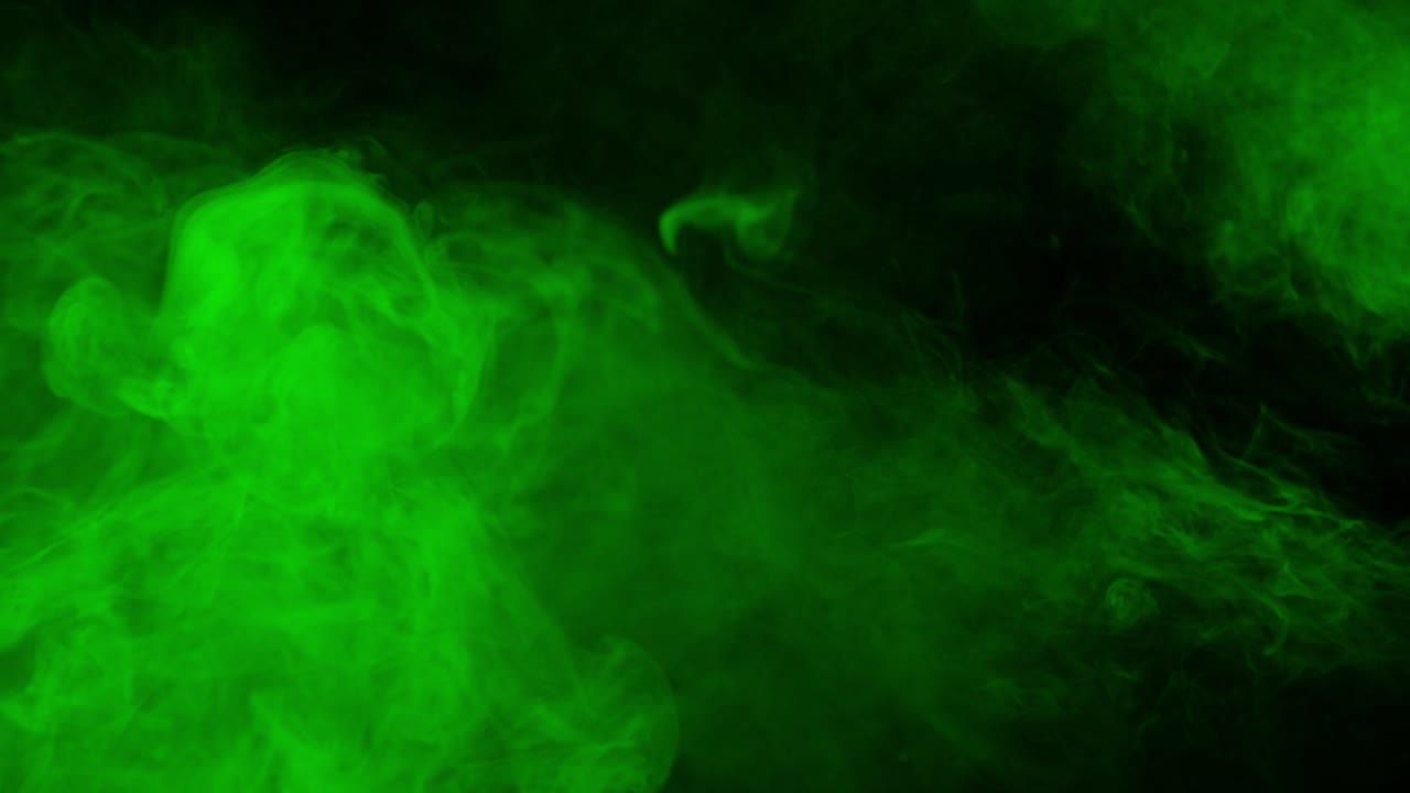 Abstract green smoke or fog slowly billows across black background, creating atmospheric and mysterious texture for overlays or transitions