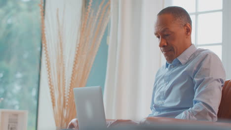 mature man or businessman working from home sitting in armchair using laptop computer