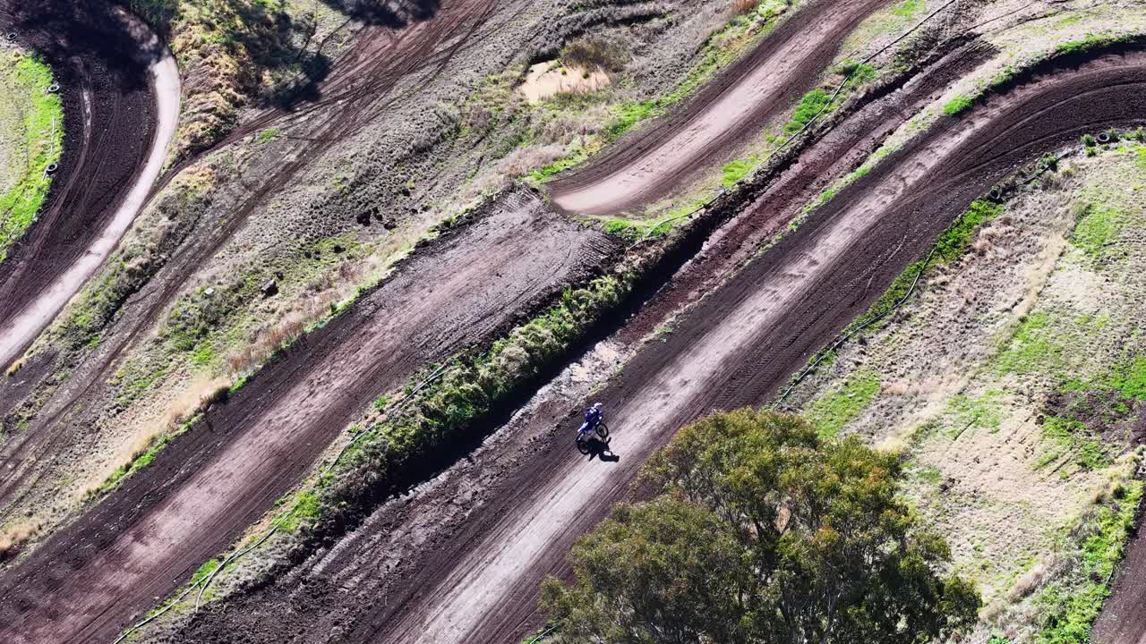 Motorcyclist rides along winding dirt track, aerial perspective, bright daylight, rural outdoor setting