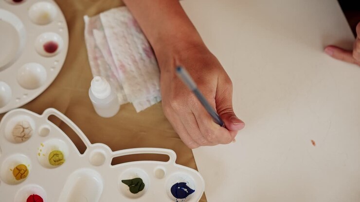 Una mano tampona delicatamente della carta acquerello con un pennello sottile, ripresa media con pullback dall'alto.