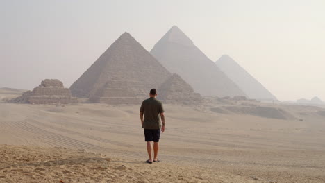 a man walking on the giza plateau with views of the pyramids at sunrise near cairo, egypt - tracking shot
