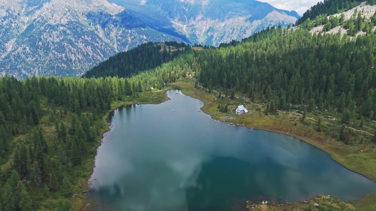 Idyllisk flygvy över San Giuliano alpsjö och Doss del Sabion-berget. Vackert landskap med en skog och en ensam stuga