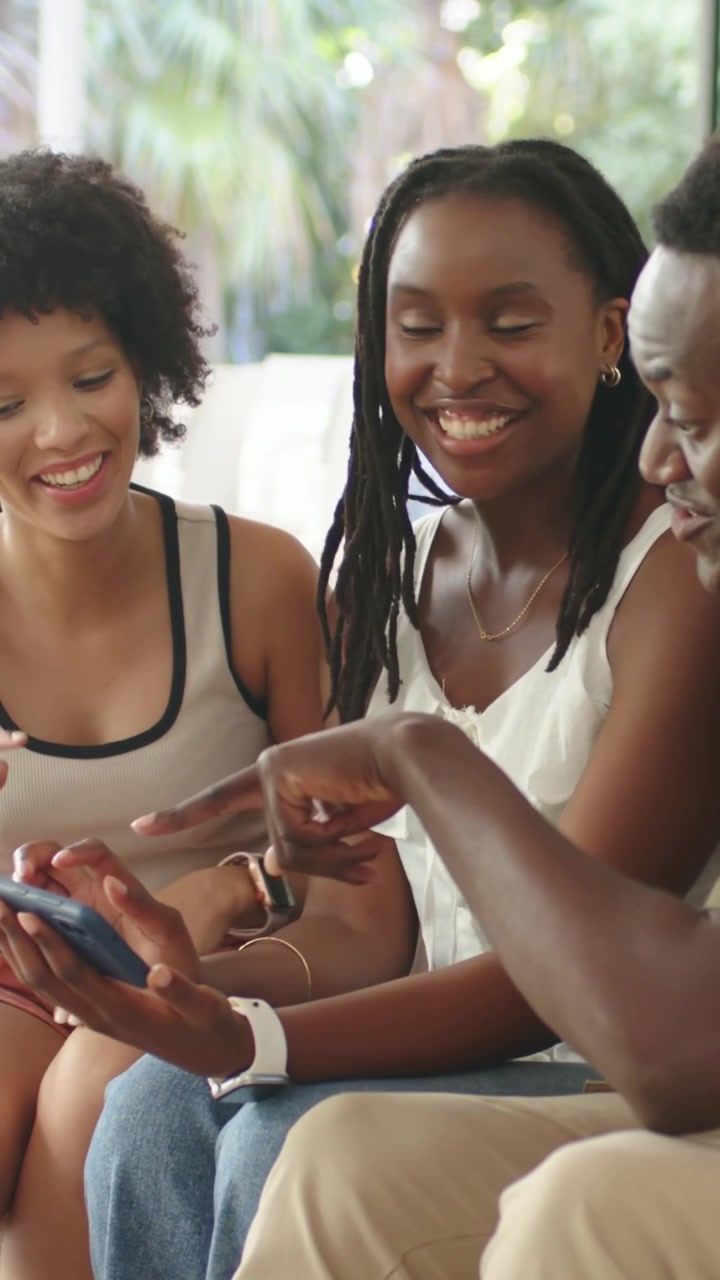 Vertical video: Holding blue phone, 3 pals leaning in viewing screen, casual, laughing on couch