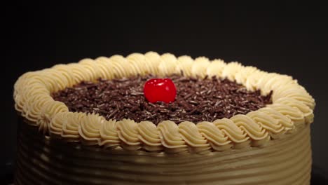 detail close up shot mocha cake in a turn table with black background mocca moka mochachino with shiny cherry on top fresh delicious tasty dessert party celebration